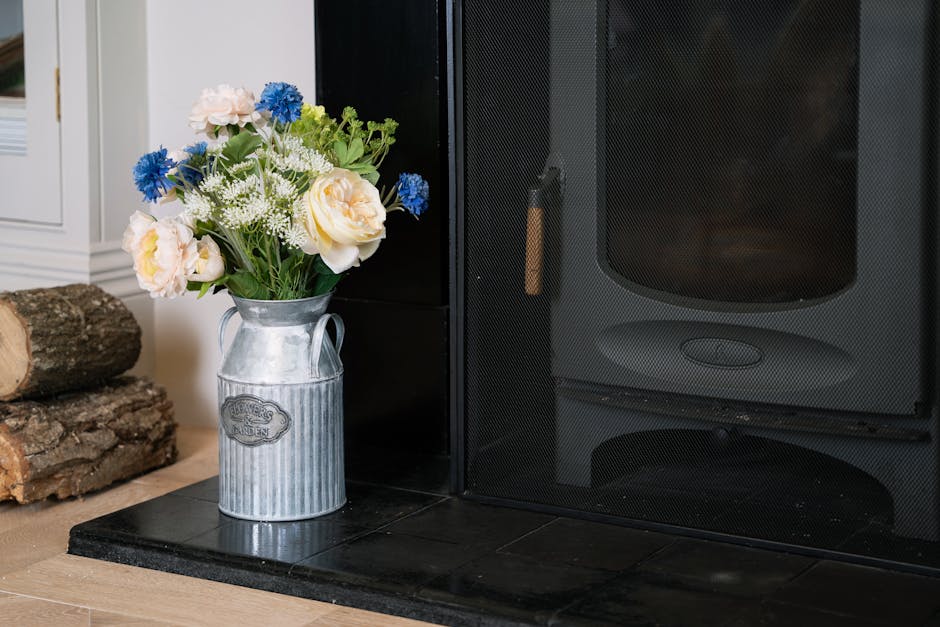 Artificial cottage garden floral arrangement by fireplace in rustic urn vase