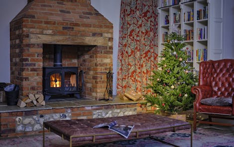 A Christmas tree in a warm room with a fireplace, bookcase, and a leather armchair