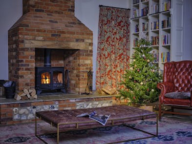 A Christmas tree in a warm room with a fireplace, bookcase, and a leather armchair