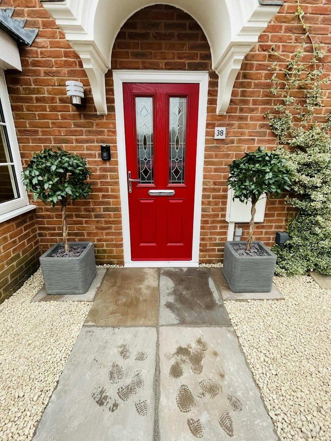 Artificial bay laurel trees either side of a red front door of house