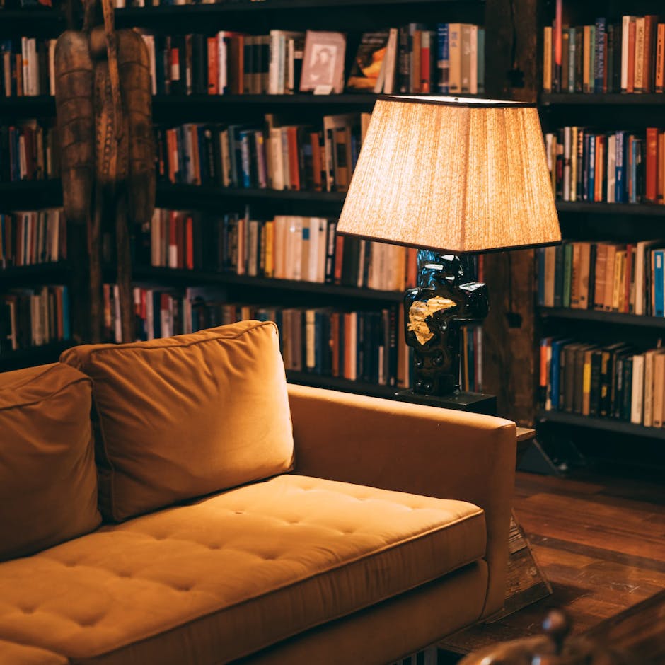 Sofa and a lampshade on a wooden floor with a bookcase behind it