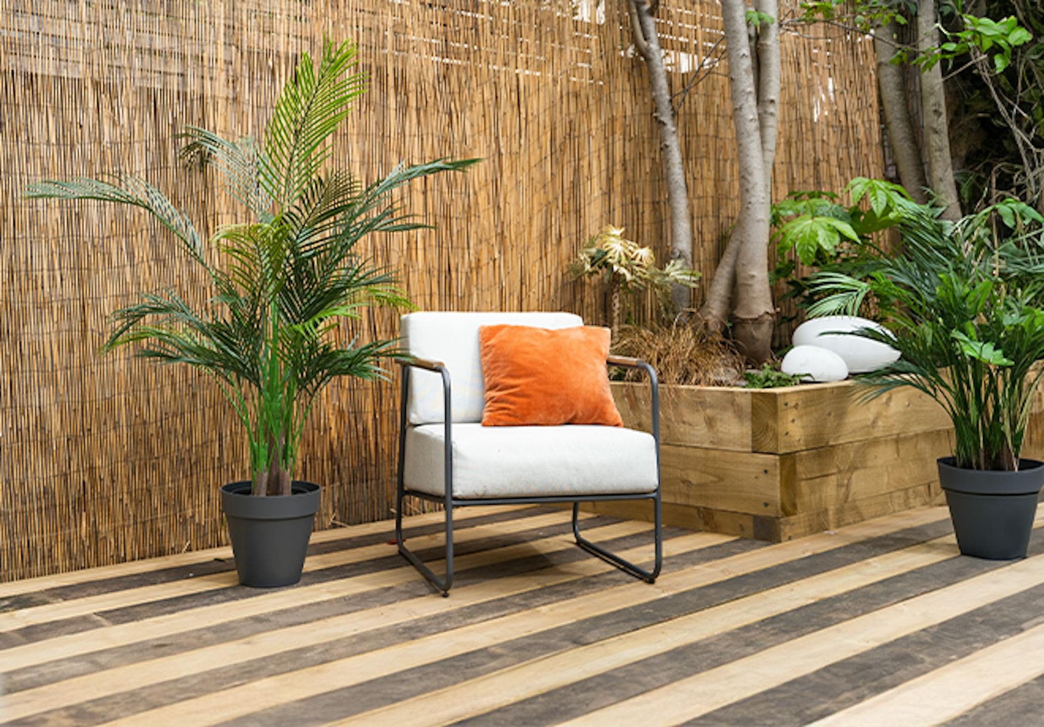 Artificial outdoor areca palm tree on garden decking with chair