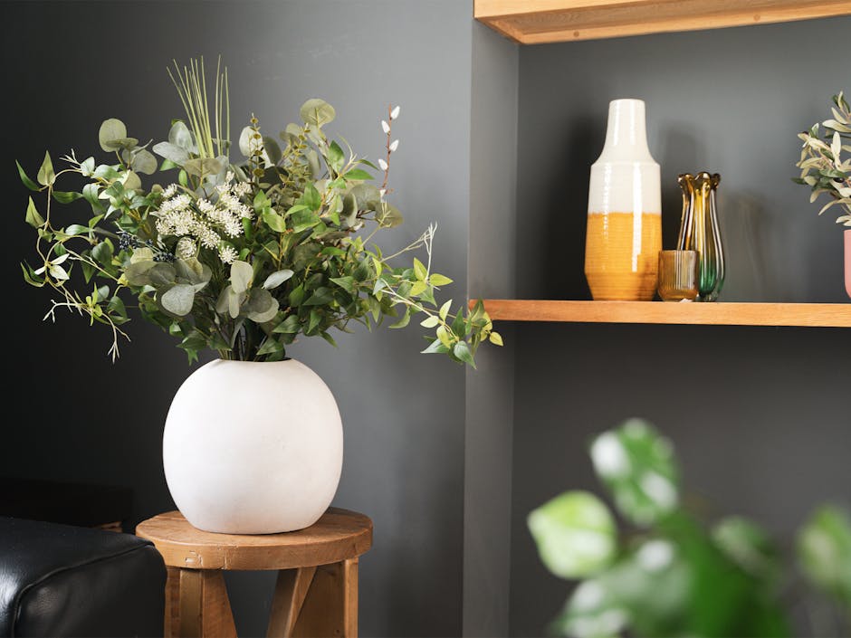 Artificial foliage bouquet in white ceramic vase on wooden side table