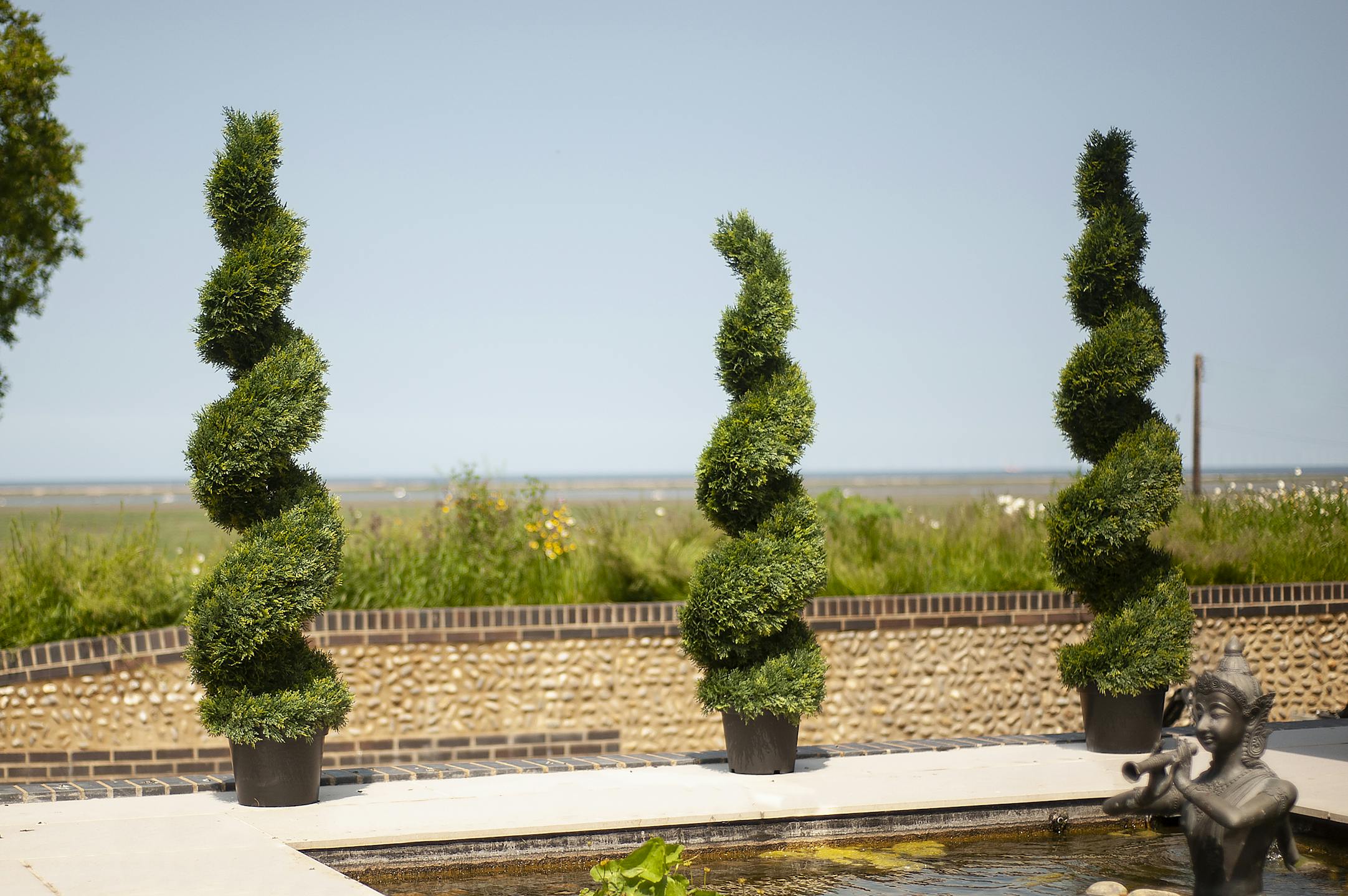 Artificial cedar spiral topiary trees by pond