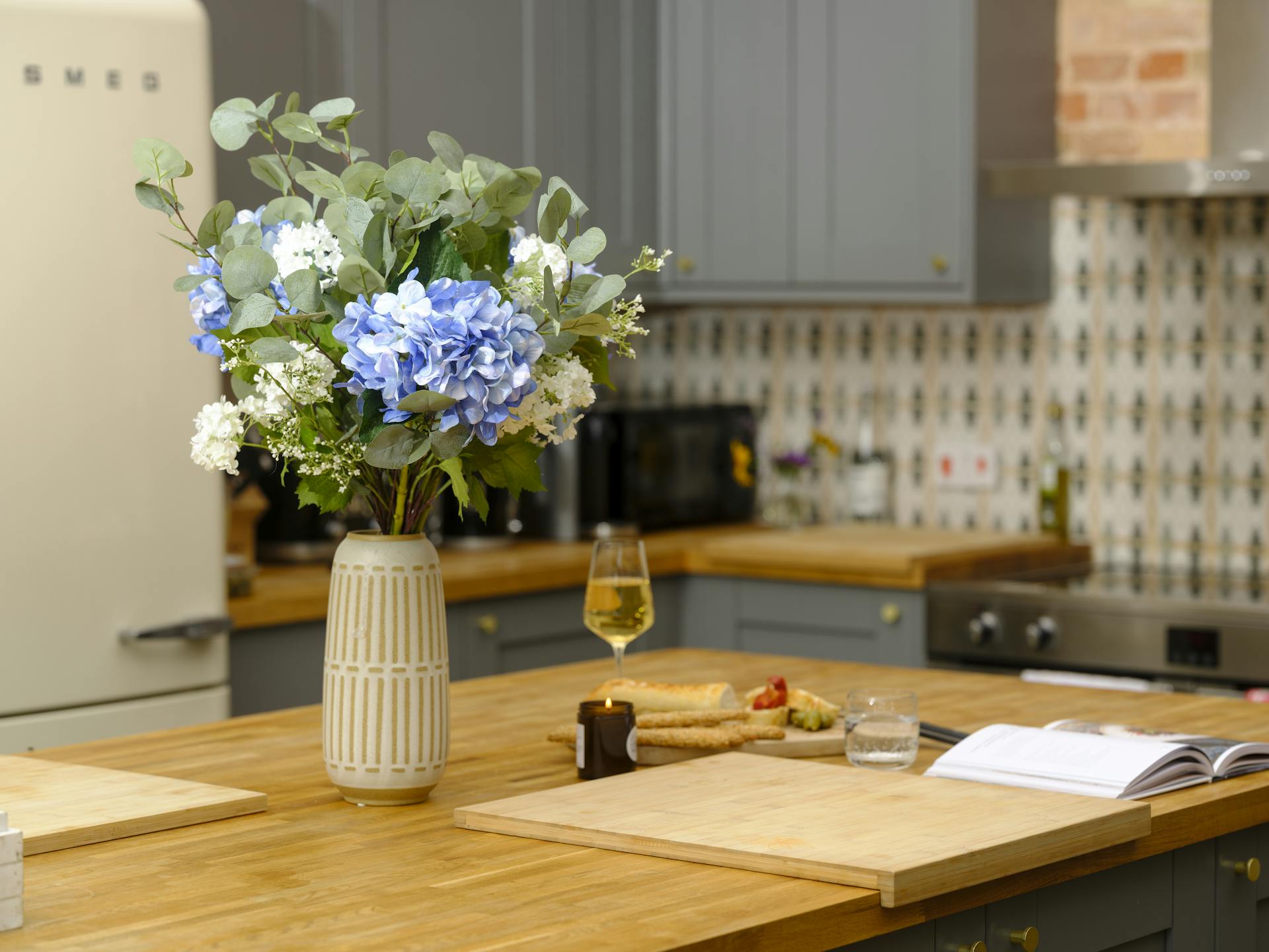 Artificial blue hydrangea bouquet on a kitchen table next to bread and wine