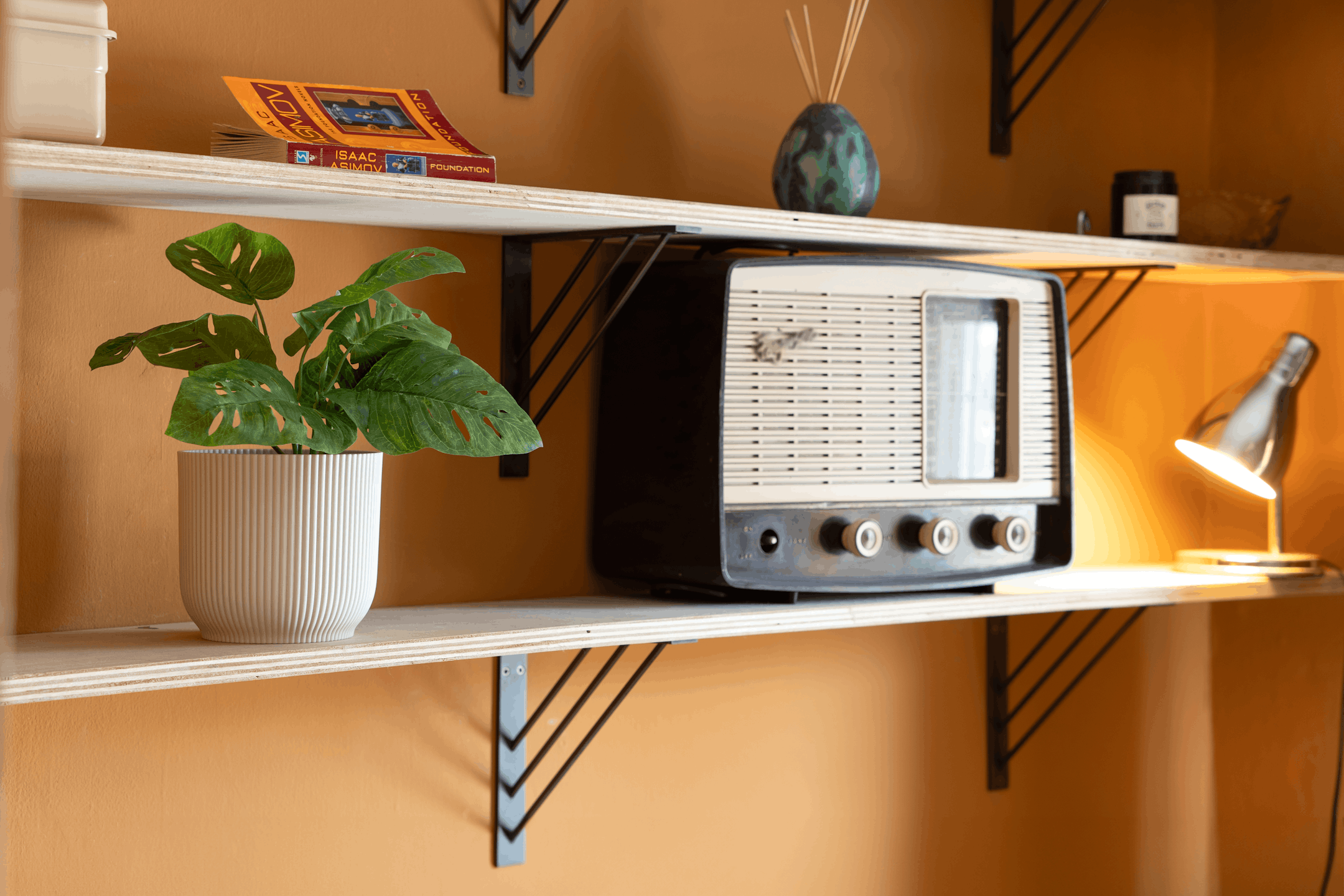 Artificial monkey monstera plant on wooden shelf in orange bedroom