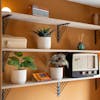 Three small artificial plants in white pots on bedroom shelves in orange room