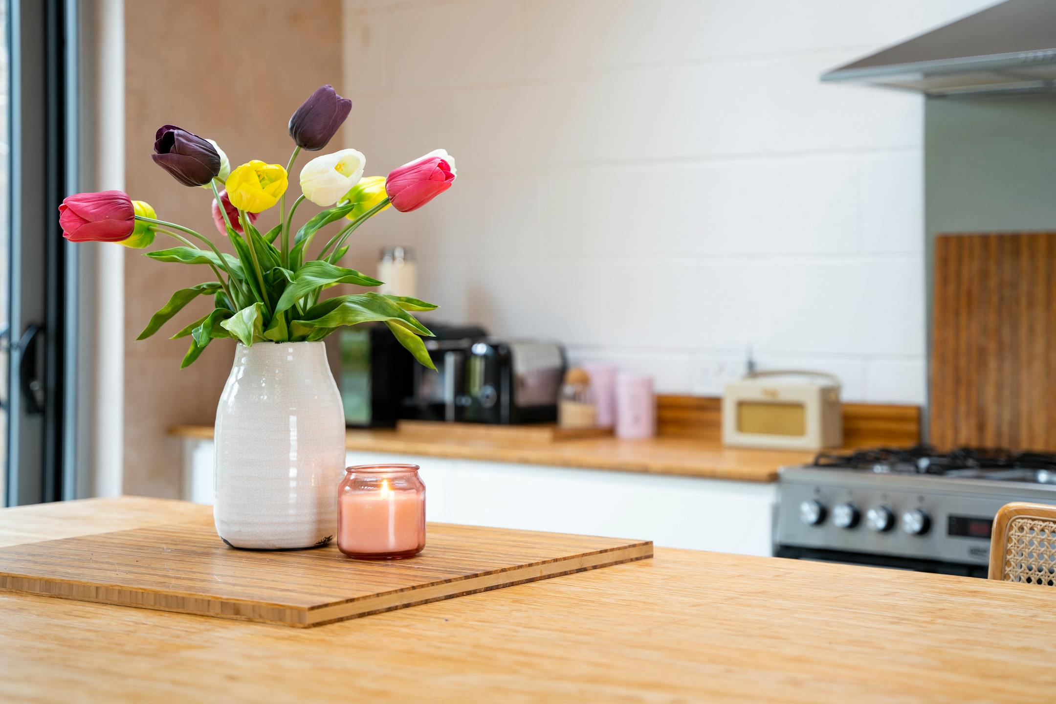 Artificial tulips bunch in white stefanie vase with pink candle on wooden kitchen island