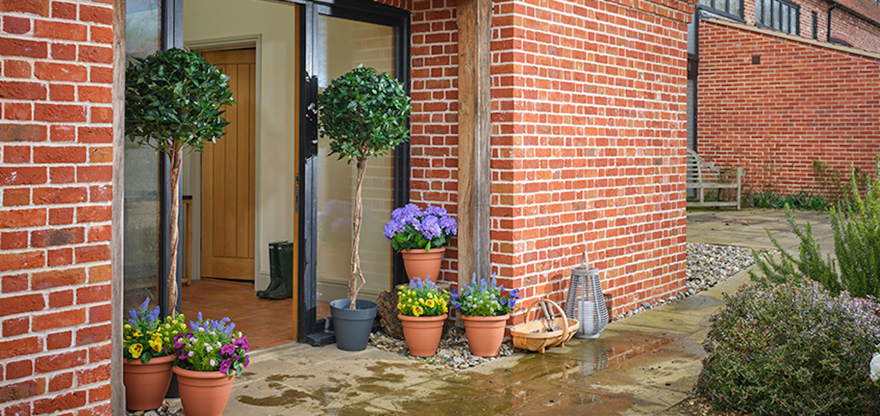 Two artificial bay trees in front of a glass door surrounded by fake flowers
