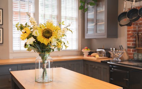 Artificial sunflower lazy days bouquet in glass vase on wooden kitchen island