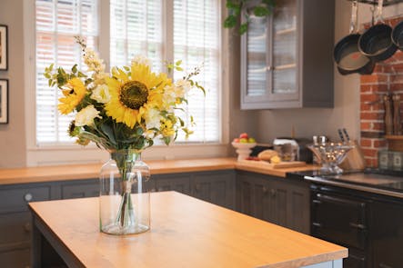 Artificial sunflower lazy days bouquet in glass vase on wooden kitchen island