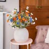 Artificial meadow bouquet in cement vase with pink chair