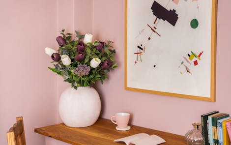 Artificial twilight bouquet in cement vase on wooden table in pink interior