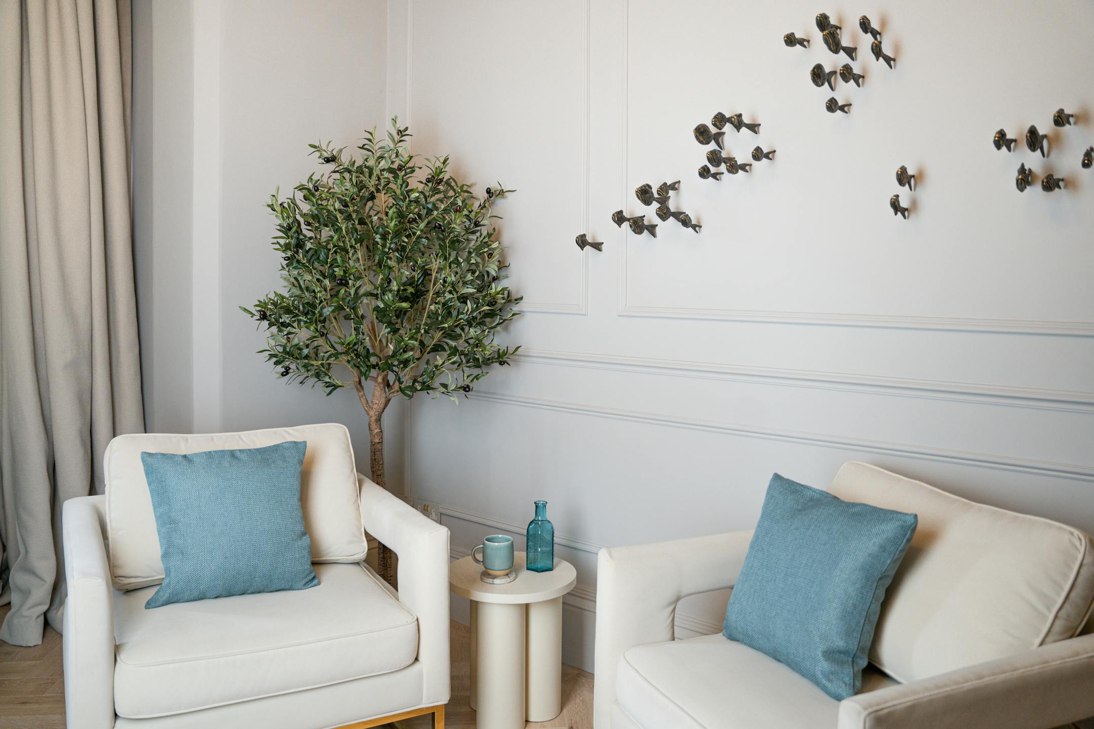 Artificial ligurian olive tree behind cream arm chair