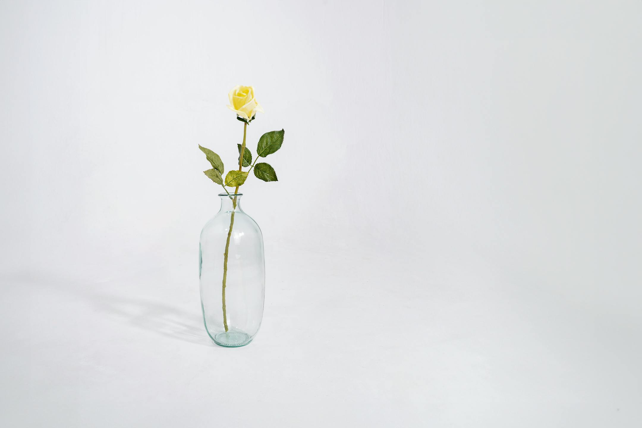 Yellow artificial rose bud stem in glass vase