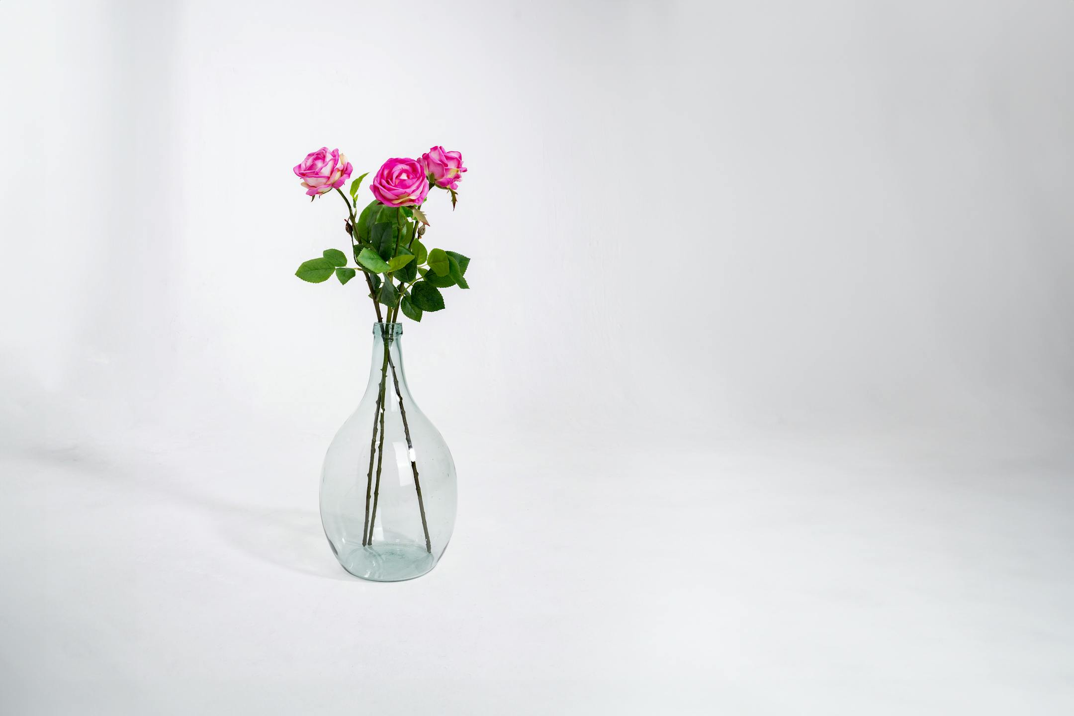 Three dark pink artificial rose stems in glass vase