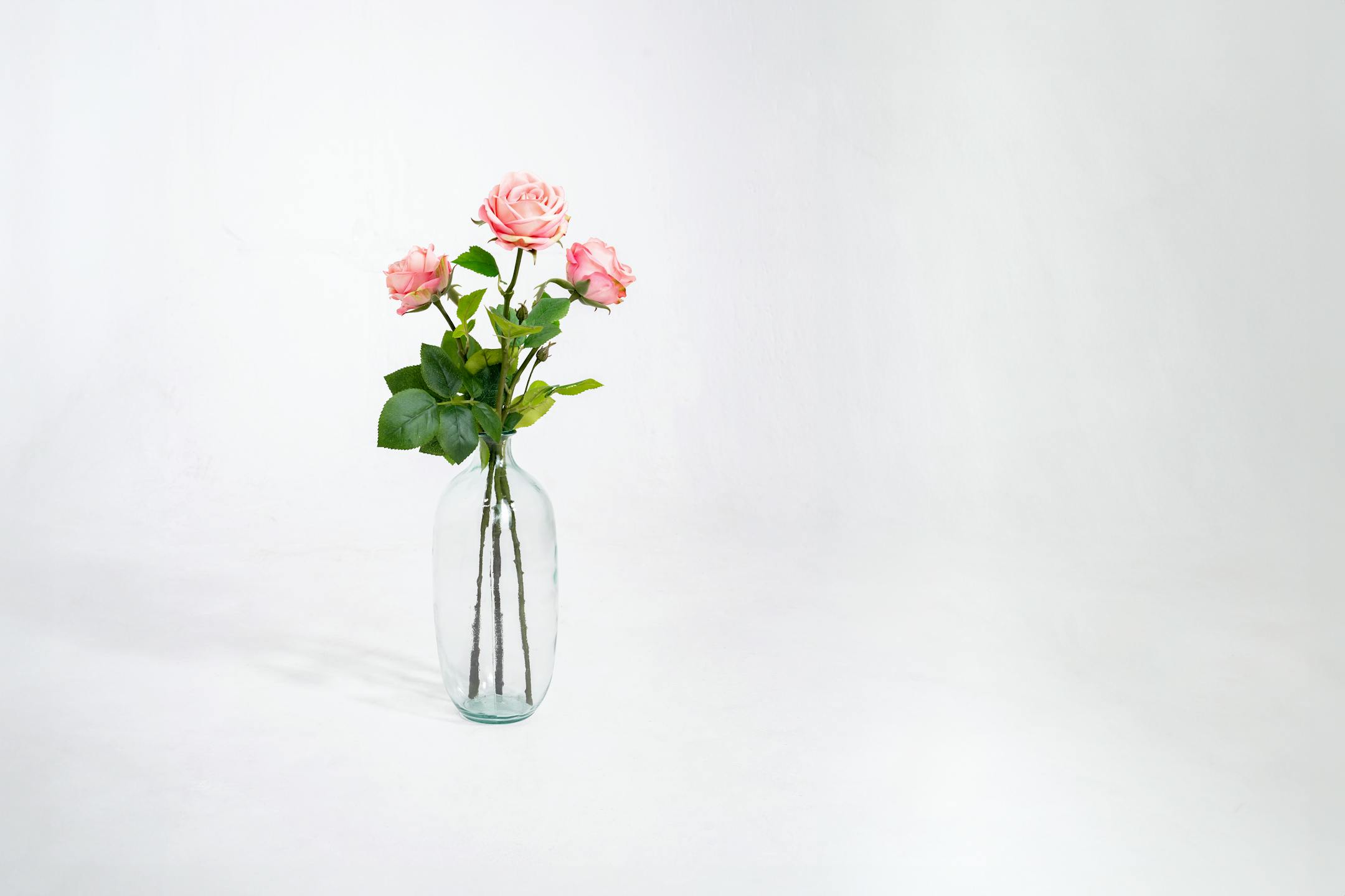 Three light pink artificial rose stems in glass vase
