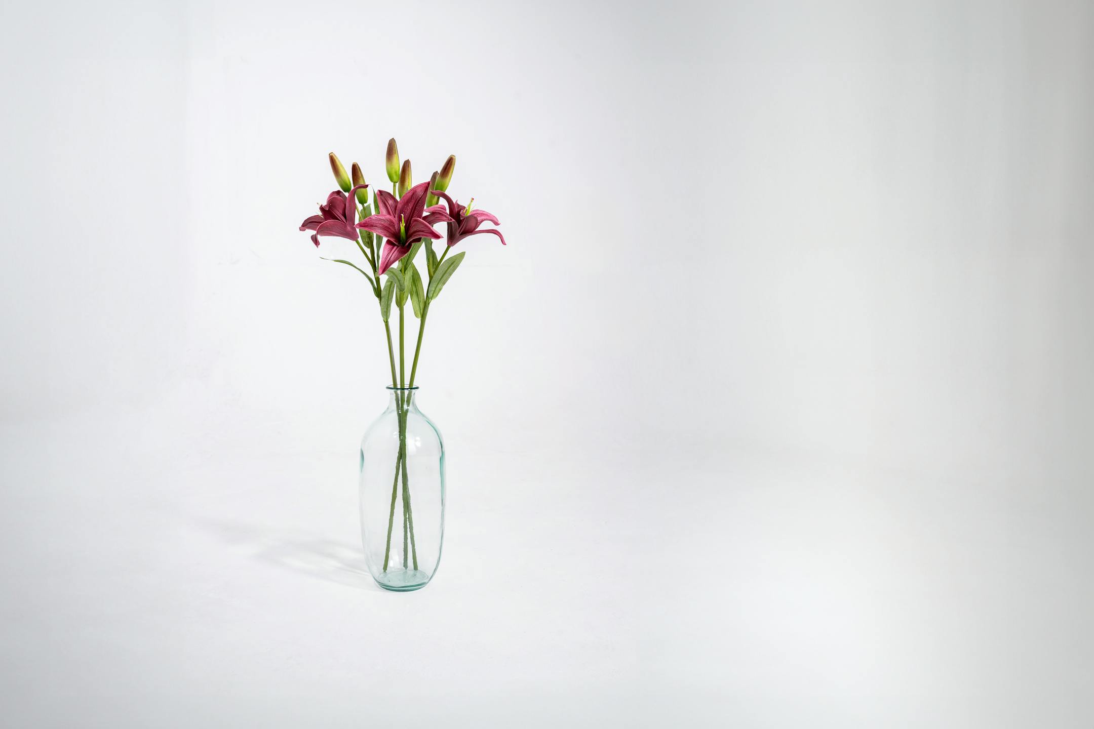 Three purple artificial lily stem in glass vase