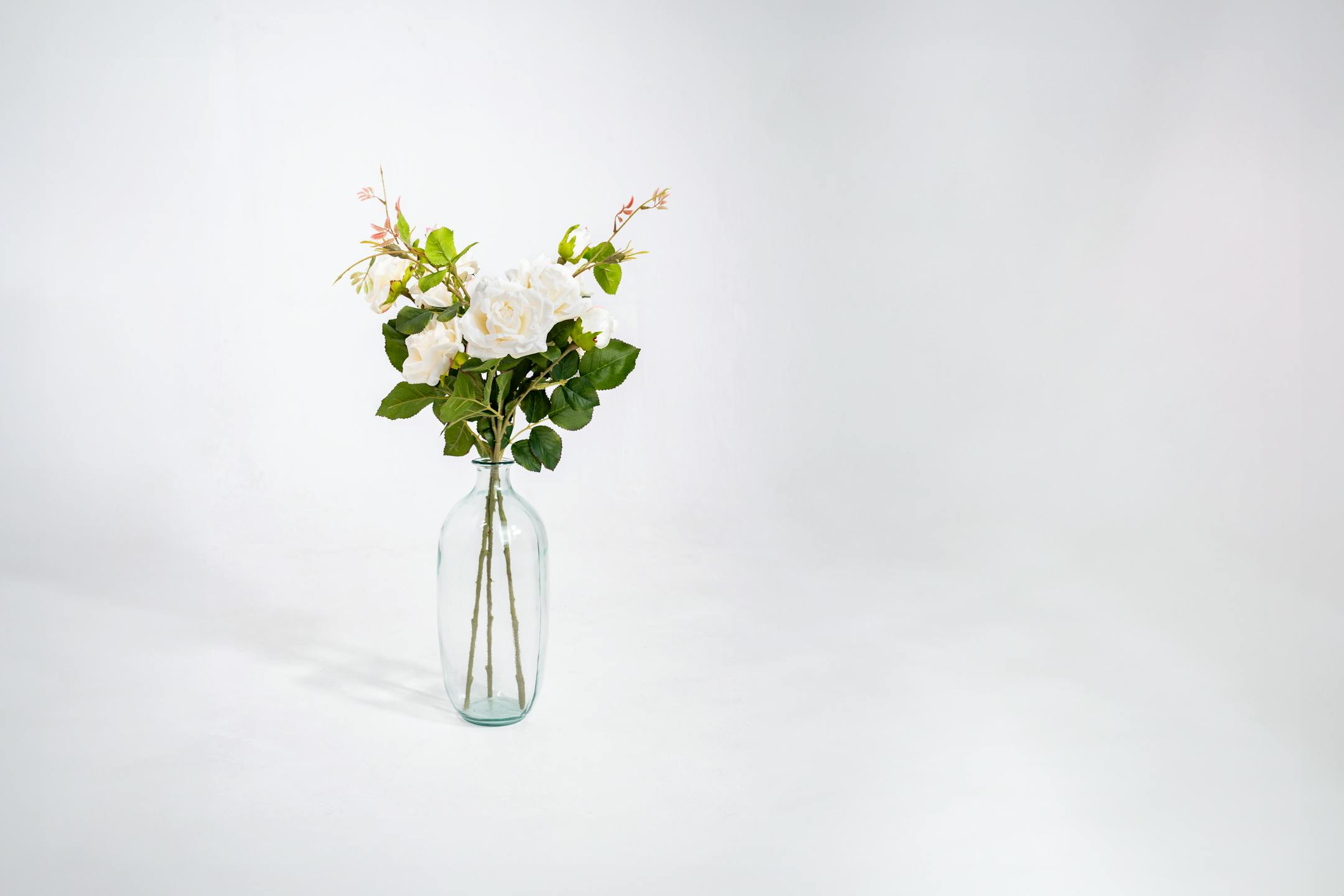 Three artificial wild rose stems in glass vase