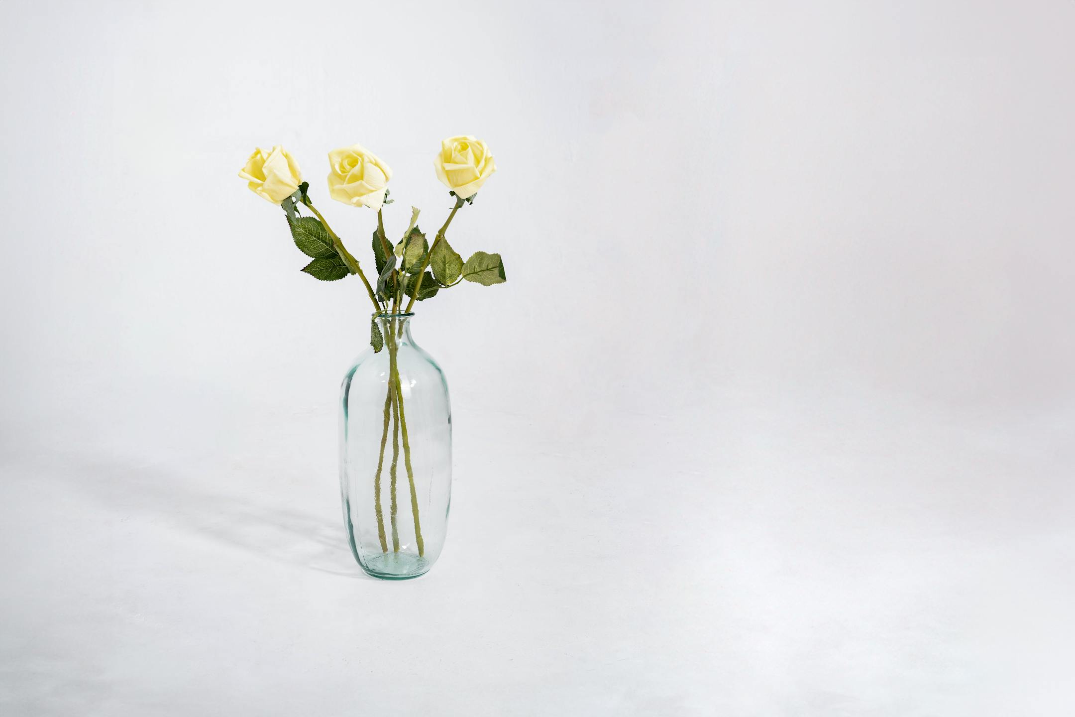 Three yellow artificial rose bud stems in glass vase