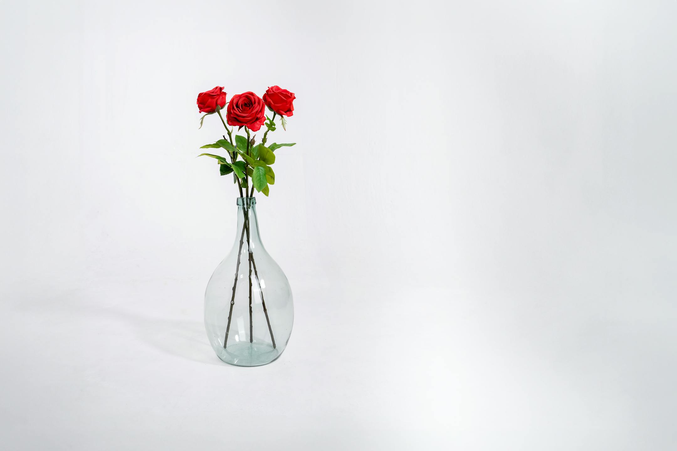Three red artificial rose stems in glass vase