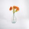 Three orange single artificial sunflower stems in glass vase