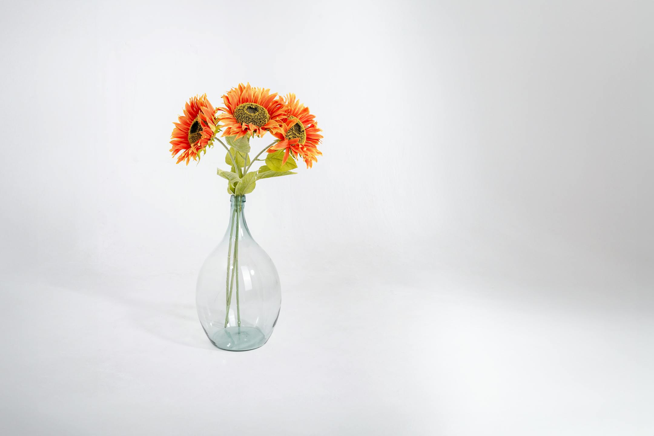 Three orange single artificial sunflower stems in glass vase