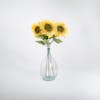 Three yellow single artificial sunflower stems in glass vase