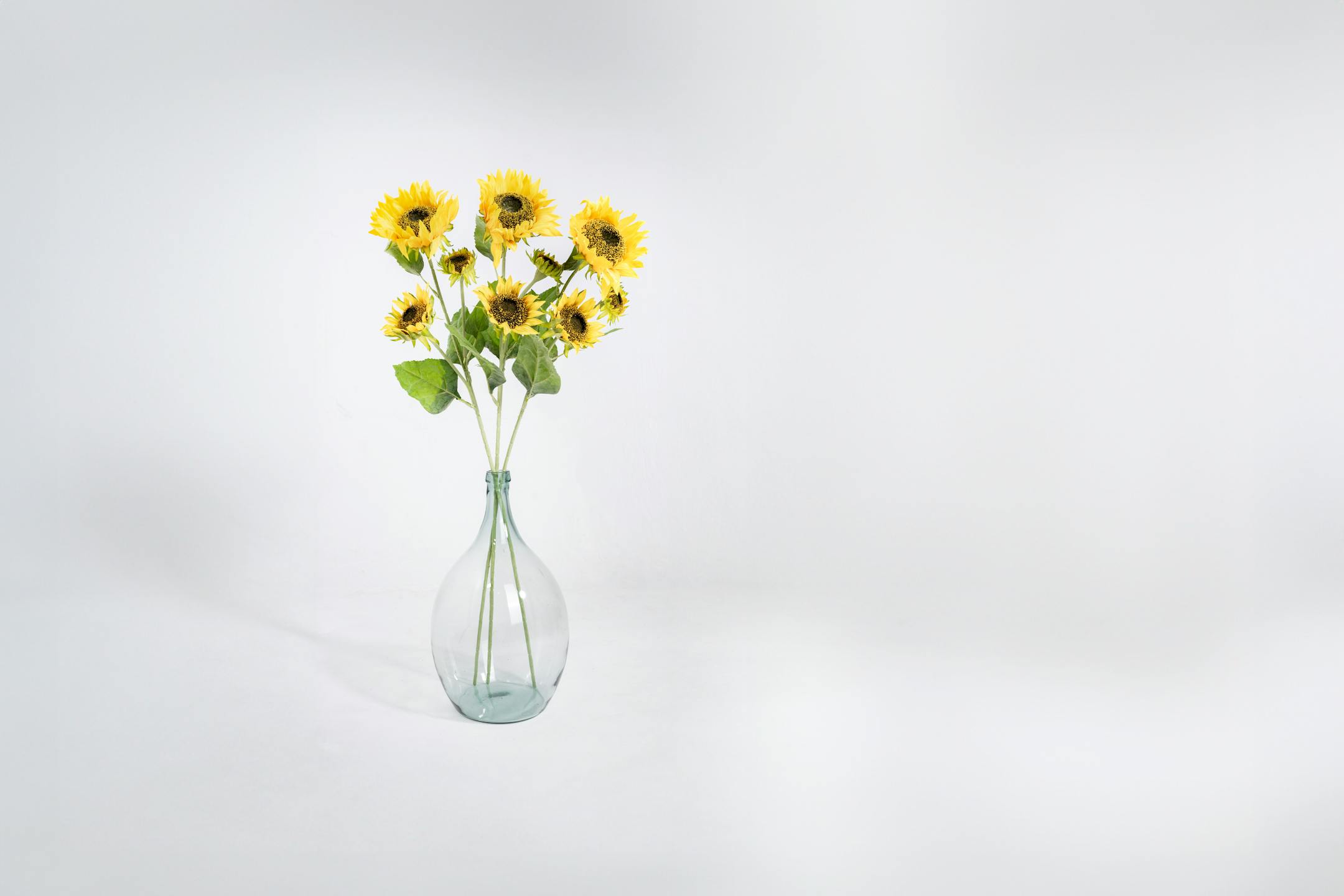 Three triple yellow artificial sunflower stems in glass vase