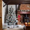 Artificial flocked balsam pine Christmas tree next to fireplace