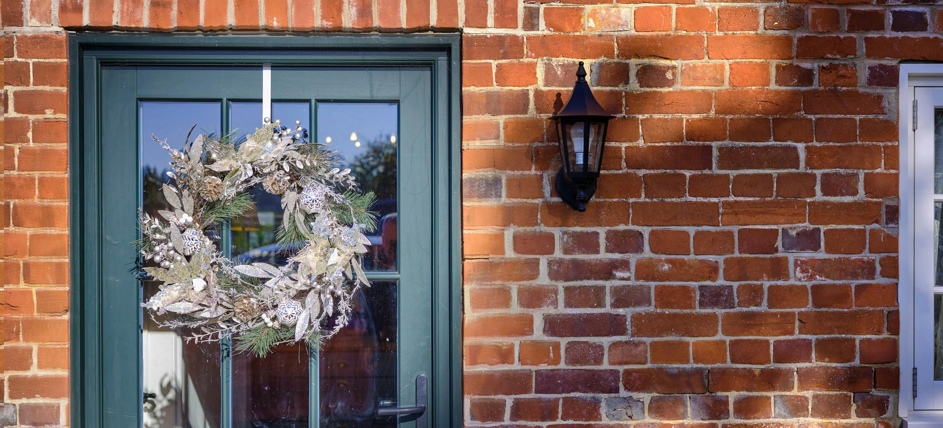 Glittery Christmas wreath hanging on green door on red brick house