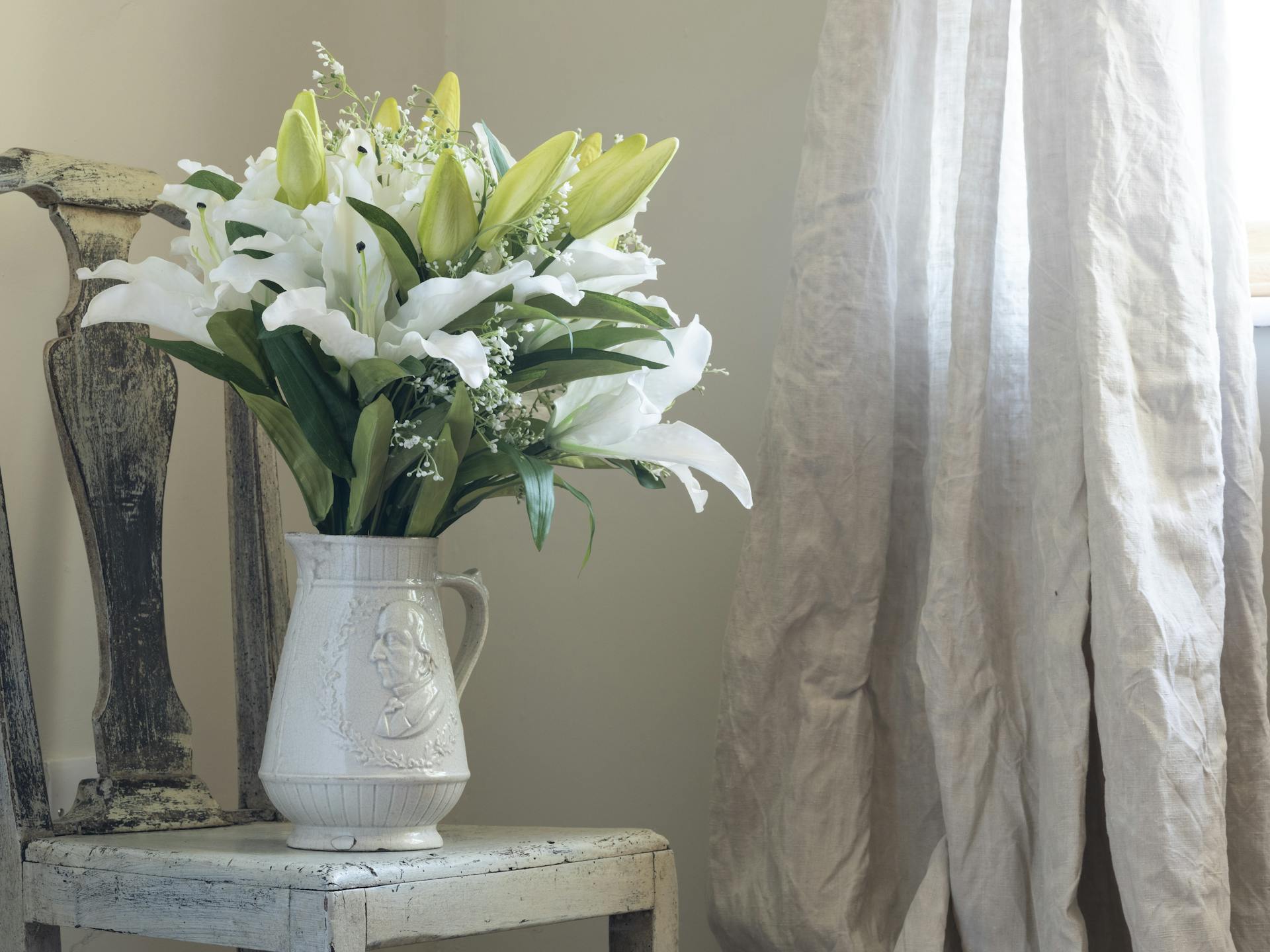 Artificial lilies in white jug on rustic chair