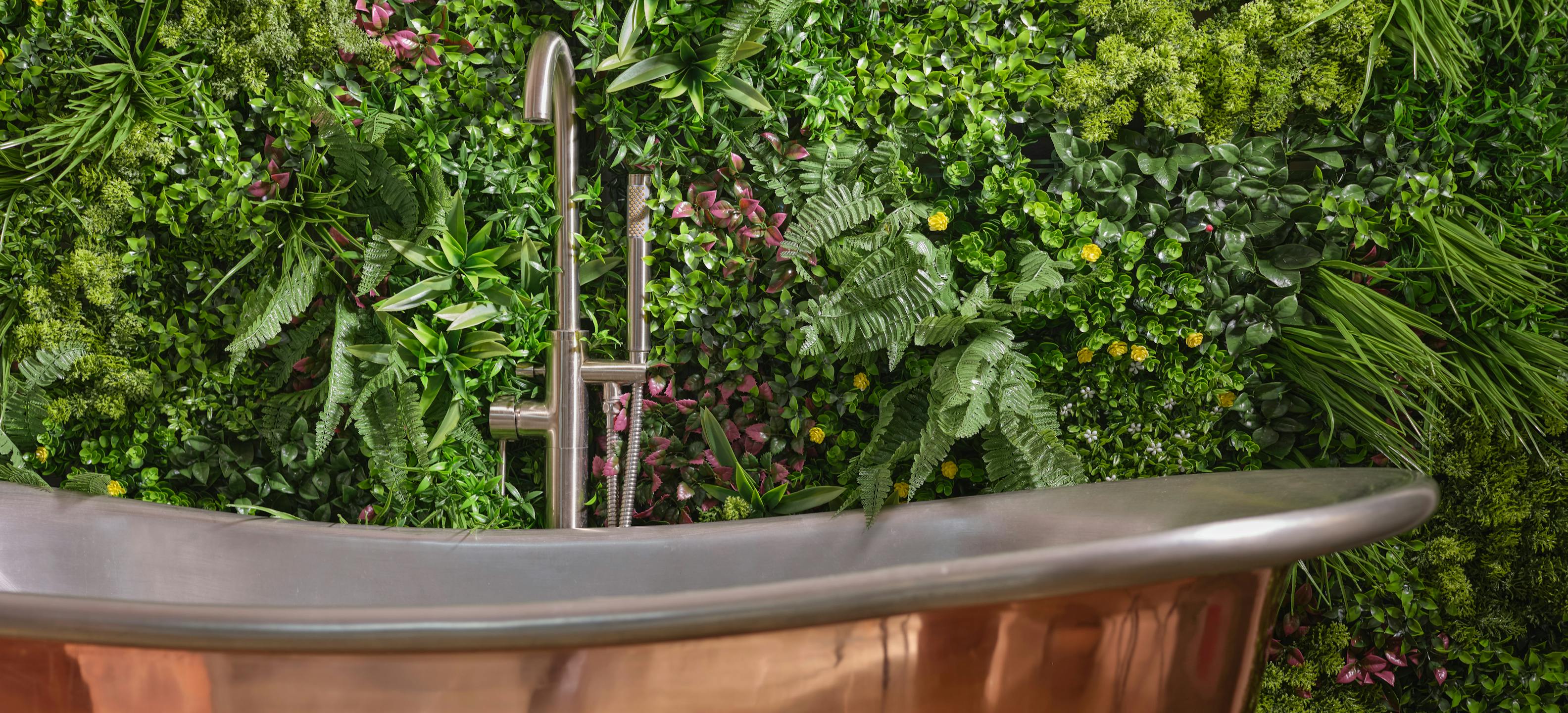 Blooming Artificial wonderland-style green wall panels behind luxury copper bath