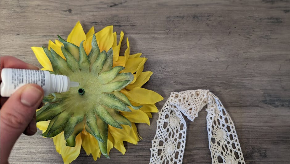 A hand applying glue to the back of the sunflower head