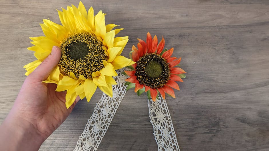 a hand placing down a yellow and orange sunflower onto the piece of ribbon