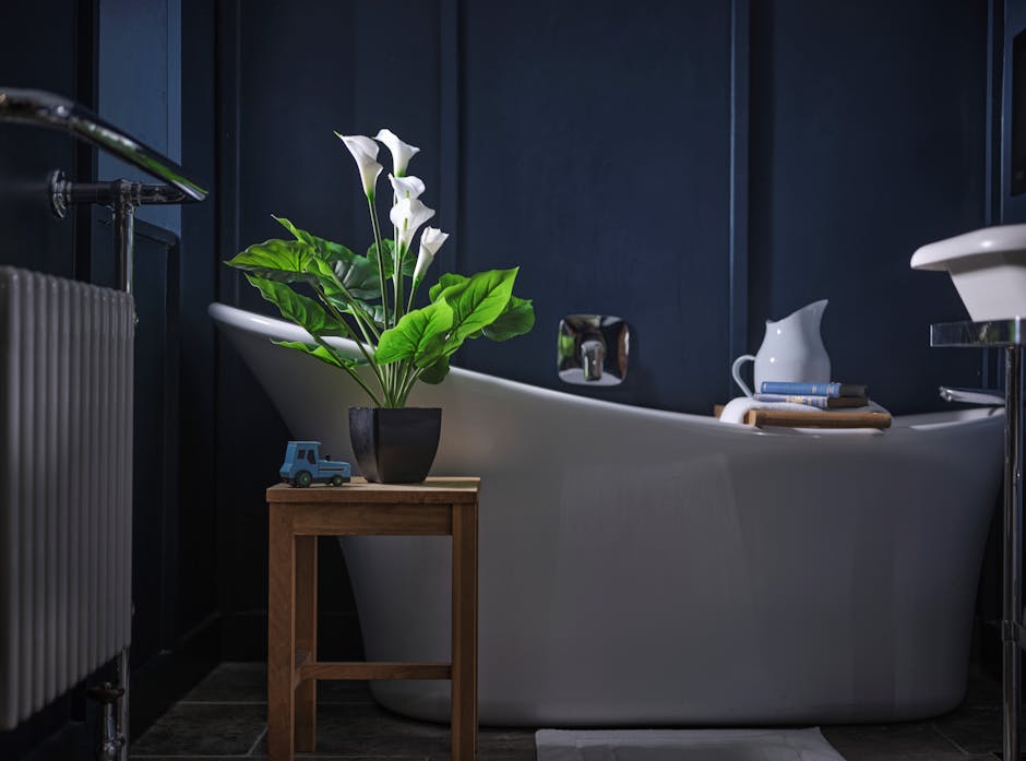 Artificial white calla lily in dark blue bathroom on small wooden table in front of bath
